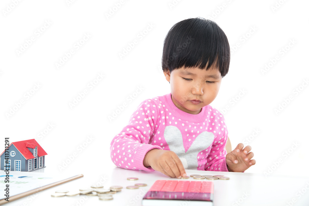 In front of the white background, the little girl is fiddling with the euro coins on the table, the calculator and the small house model on the table In front of the white background, the little girl is fiddling with the euro coins on the table, the calculator and the small house model on the table