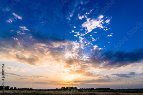 summer morning landscape with colorful sunrise and sun rays in the sky with clouds over the meadow © alexkoral