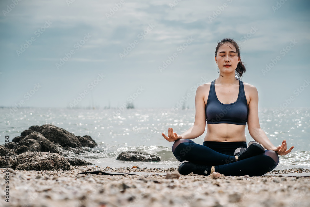 Asian fitness runner body closeup doing warm-up routine on beach before running, stretching leg muscles with standing single knee to chest stretch. Female athlete preparing legs for cardio workout.