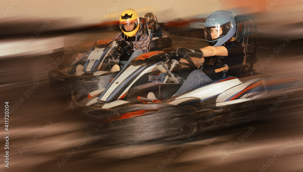 Group of positive smiling people driving go-carts at racing track