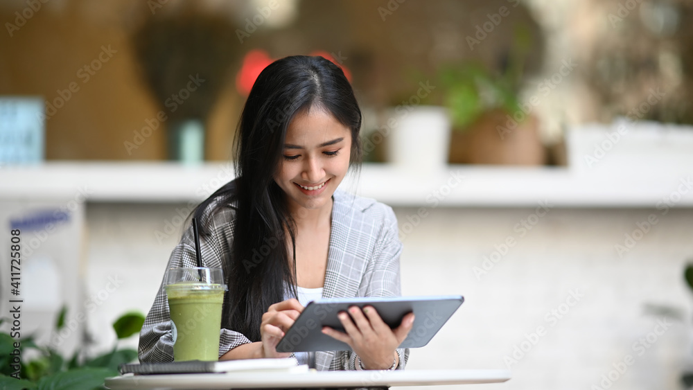 Smiling young businesswoman working with digital tablet and sitting at cafe with healthy vegetable drink. Smiling young businesswoman working with digital tablet and sitting at cafe with healthy vegetable drink.
