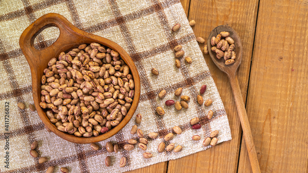 Borlotti beans in wooden bowl and spoon on wooden table with checkered cloth, top view Borlotti beans in wooden bowl and spoon on wooden table with checkered cloth, top view