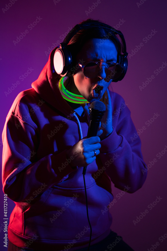 cyberpunk woman in a hooded hoodie and sunglasses dances against a wall with neon sticks hanging around her neck