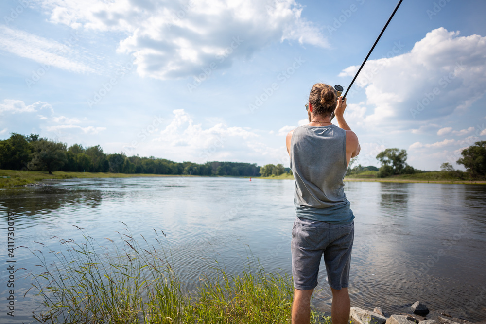 Young fisher on a river bank casting a fishing rod Young fisher on a river bank casting a fishing rod