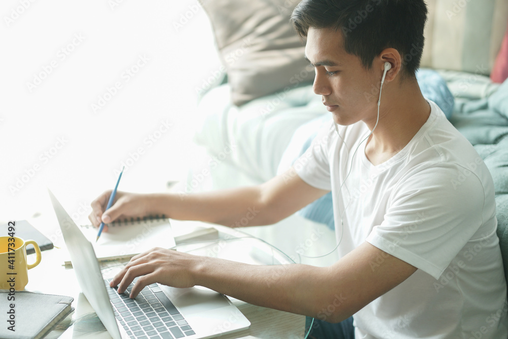 Obraz premium asian young student man entrepreneur wear earphones working with computer studying learning online at home. e-learning webinar meeting. social distance in covid pandemic