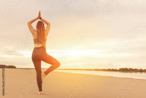 Silhouette of an authentic young woman doing yoga on the beach  standing in a tree pose at sunset. healthy lifestyle concept. copy space