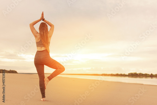 Silhouette of an authentic young woman doing yoga on the beach, standing in a tree pose at sunset. healthy lifestyle concept. copy space