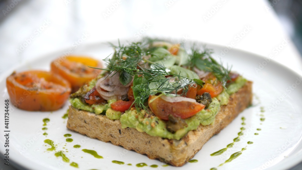 Hand serving avocado toast decorated with vegetables. Healthy vegan breakfast 