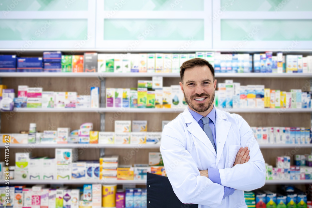 Portrait of handsome pharmacist standing in drugstore with shelf full of medicines in background.