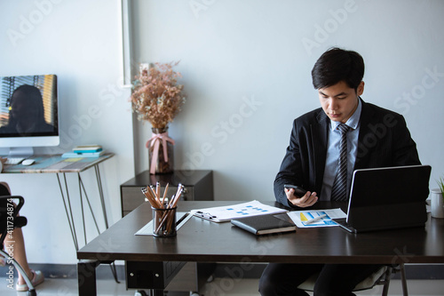 Young Asian businessman Sitting and working at a desk With market analysis sheet, Tablet, PC