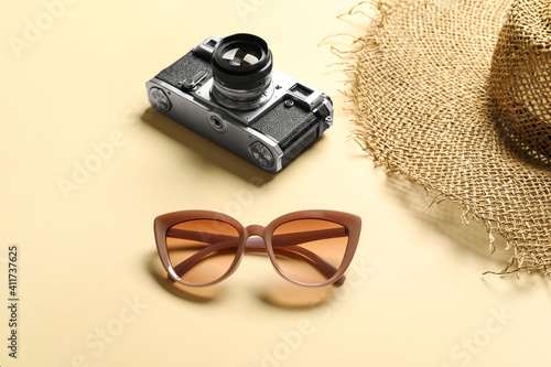 Stylish sunglasses, photo camera and hat on color background