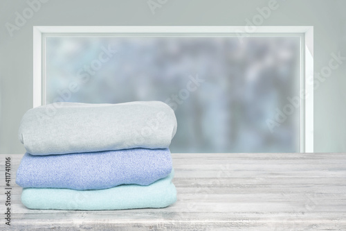Stack of winter clothes. Pile of colorful knitted cozy warm cashmere sweaters or pullover on wooden table against abstract bright winter background. Space for display product montage. Beautiful backdr