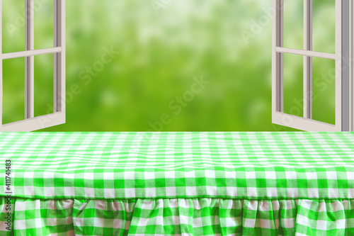 Empty table product. Empty wooden deck table covered with a green white checkered tablecloth over abstract blurred natural backdrop. Space for your food and product display montage.
