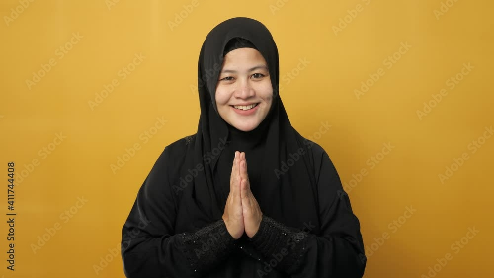 Asian muslim lady smiling and shows greeting gesture against yellow background, concept of islamic celebration of ramadan or eid fitr Asian muslim lady smiling and shows greeting gesture against yellow background, concept of islamic celebration of ramadan or eid fitr