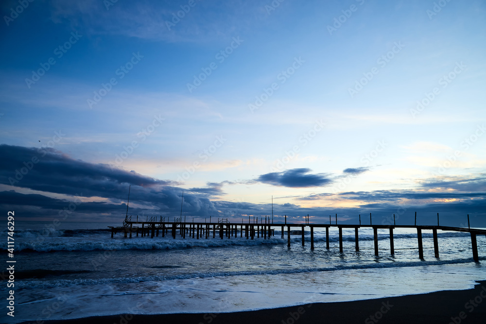 Obraz premium View from beach to water of sea, waves with white foam, pierce and sky with clouds in a nice evening.