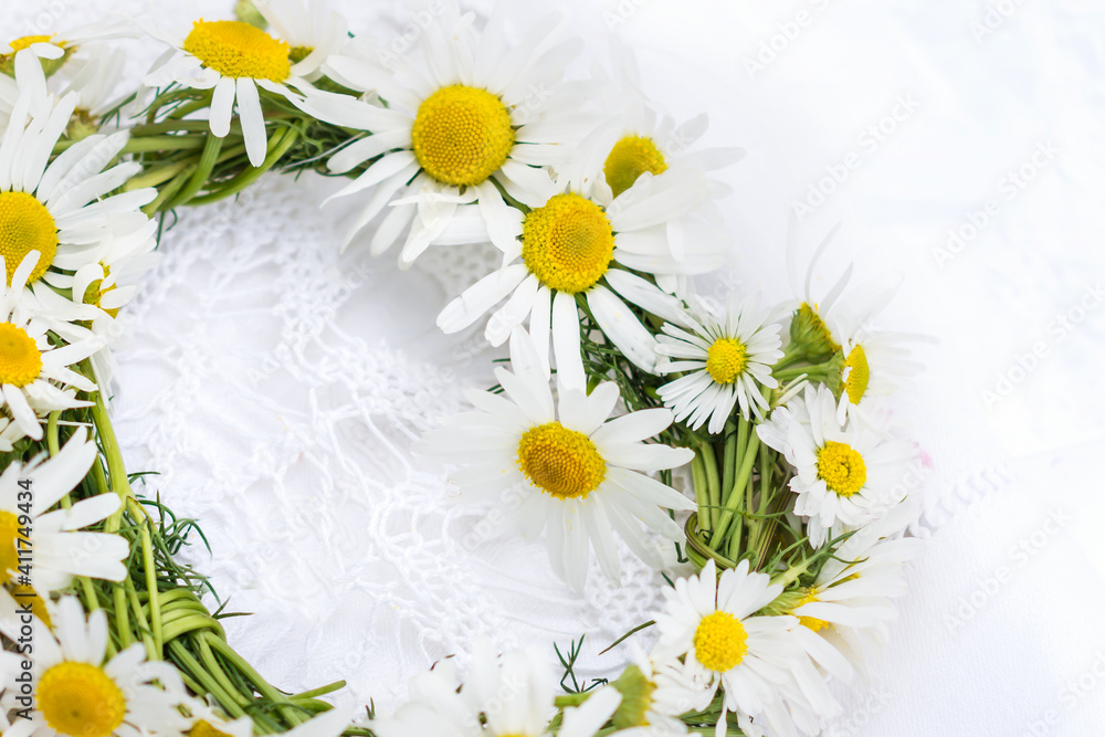 Obraz premium Wreath of chamomile flowers on white crochet napkin and white background, handmade vintage wreath of wild meadow flowers 