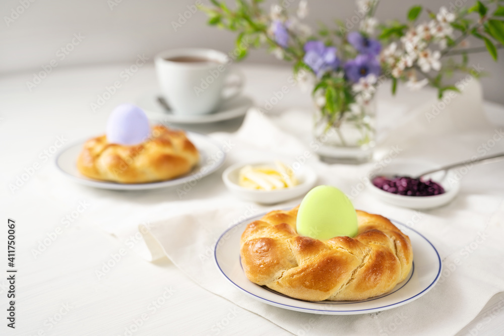 Easter breakfast with plaited yeast bread nests and colored eggs, coffee, butter, jam and flowers on a white table, copy space Easter breakfast with plaited yeast bread nests and colored eggs, coffee, butter, jam and flowers on a white table, copy space