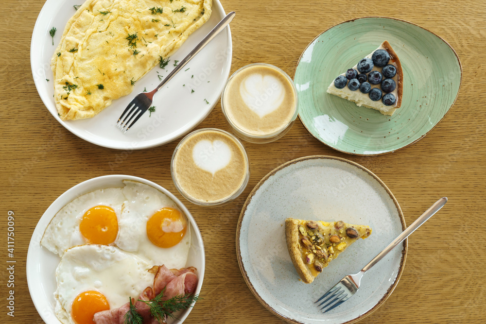 Bright breakfast on brown wooden background, top view. Tasty desserts, omelette and fried eggs and cup of coffee. Bright breakfast on brown wooden background, top view. Tasty desserts, omelette and fried eggs and cup of coffee.