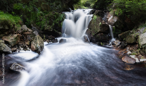 Hidden waterfall in the middle of forest. Pure natural scene. Clean nature. Flowing falling water  stones and grass surrounding the river.