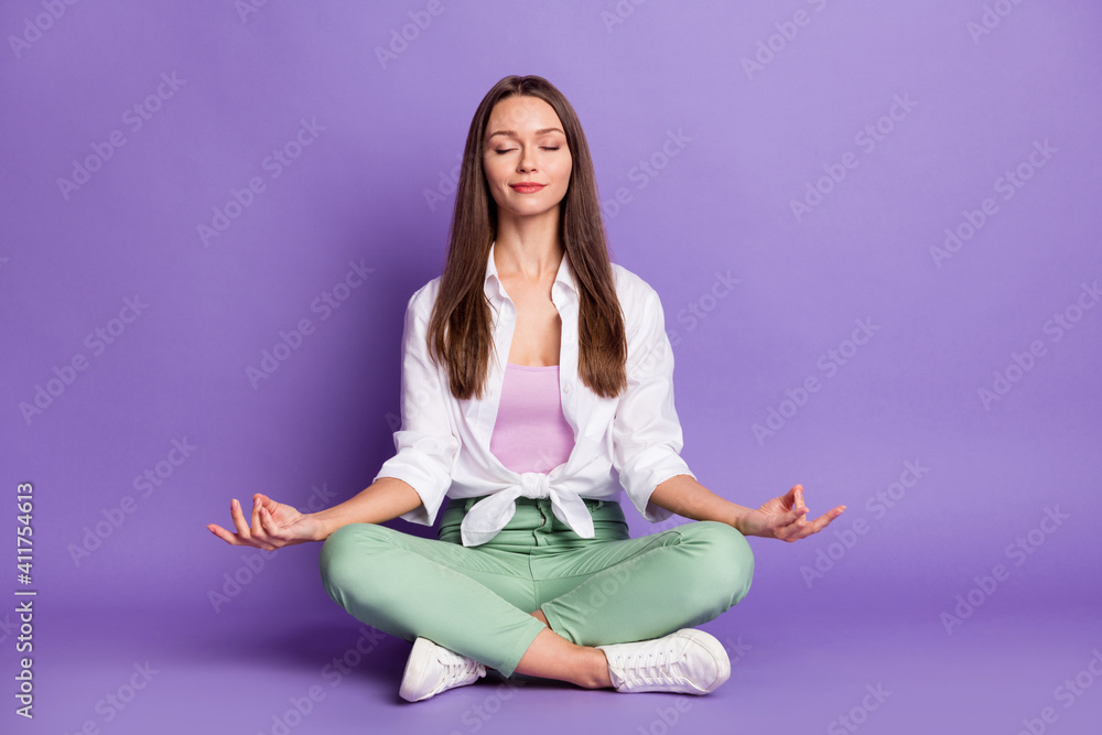Photo portrait full body view of girl sitting in lotus pose meditating isolated on vivid purple colored background Photo portrait full body view of girl sitting in lotus pose meditating isolated on vivid purple colored background