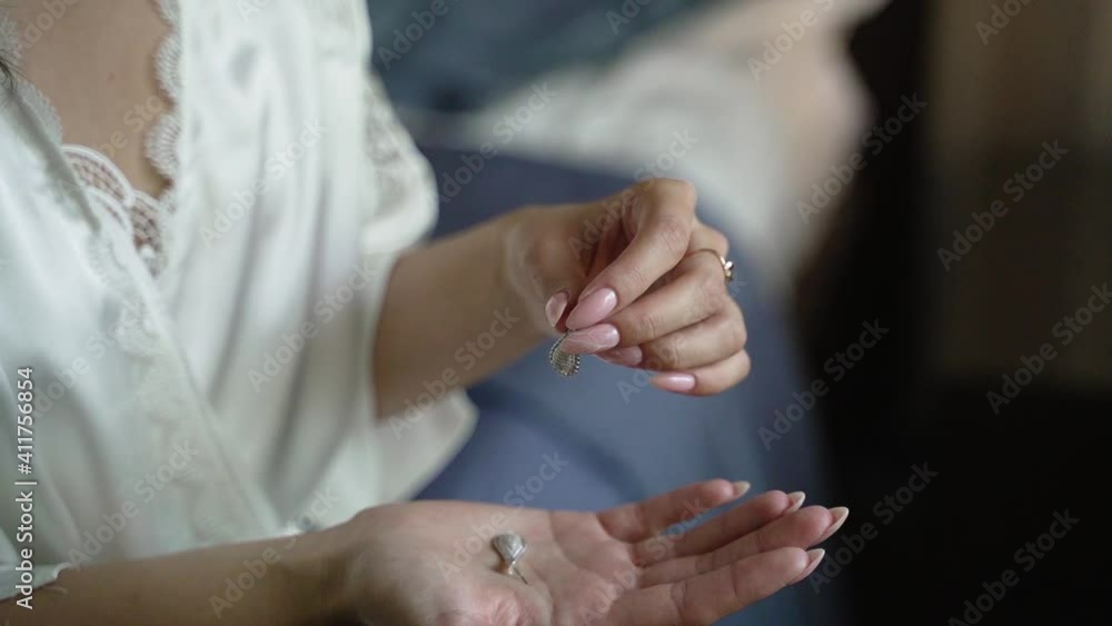 Young woman in white robe holds jewelry in her hands. Earrings in the hands of bride Young woman in white robe holds jewelry in her hands. Earrings in the hands of bride