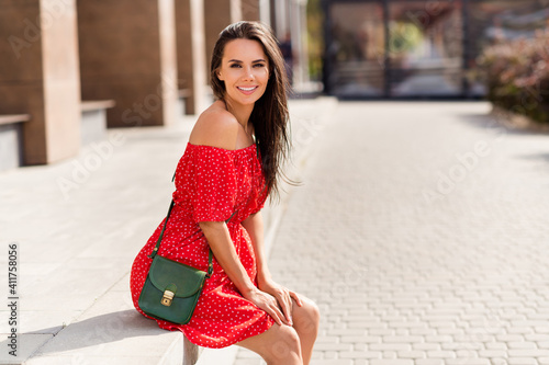 Photo of cute young woman dressed red off-shoulders dress handbag sitting stairs outdoors street city urban