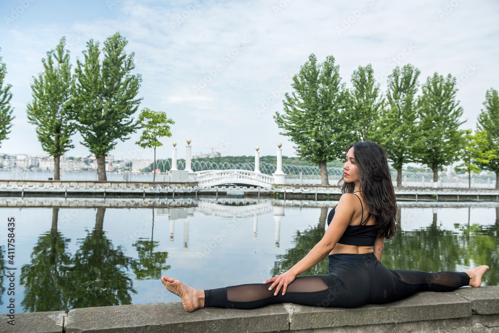 female athlete sitting on a twine and doing stretching by lake in summer day female athlete sitting on a twine and doing stretching by lake in summer day
