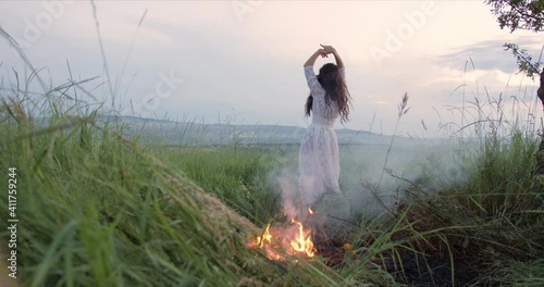 young woman is dancing near the bonfire at the sunset