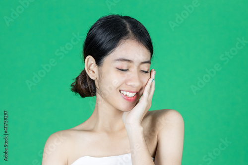 Beauty young Asian woman touching her face over green isolated background. Healthy skin care concept.