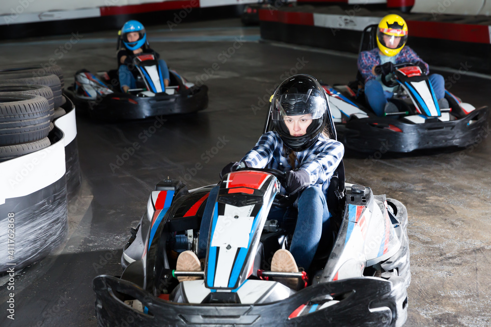 Group of male and females in helmets driving racing cars at kart track. - obrazy, fototapety, plakaty 