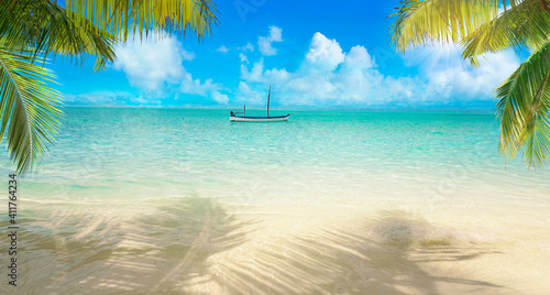 Beautiful summer landscape of tropical island with boat in ocean. Blue sky and bright sun. Transition of sandy beach into turquoise water.