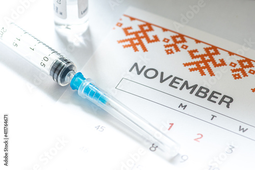 Syringe, vial and calendar with month of November on a white table ready to be used. Covid or Coronavirus vaccine background photo