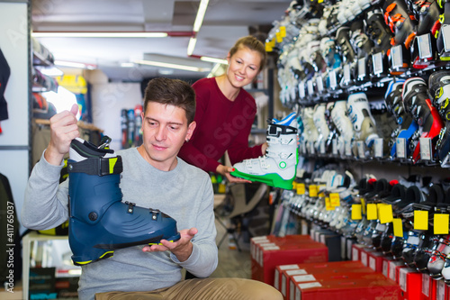 Woman assistant is helping man to trying on ski boots in store.
