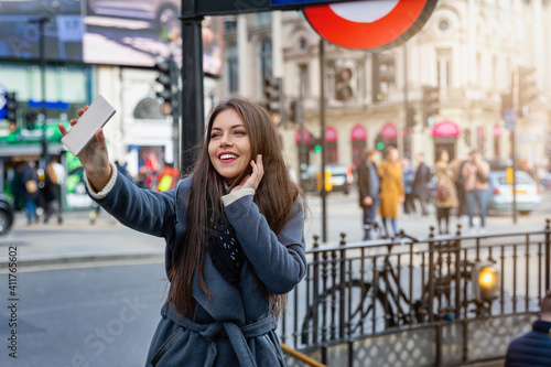 A smiling, brunette woman takes selfie photographs with her mobile phone on a st фототапет