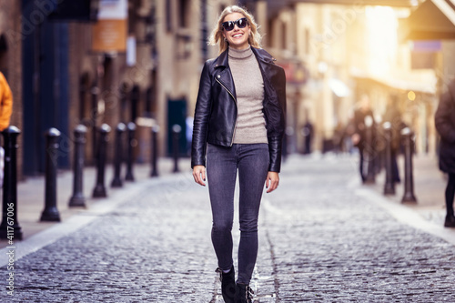 Photography A blonde urban girl with black leather jacket and sunglasses walks down the stre