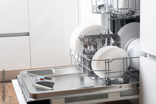 Open dishwasher with clean dishes in the white kitchen photo