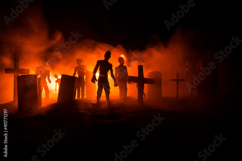 Scary view of zombies at cemetery dead tree, moon, church and spooky cloudy sky with fog, Horror Halloween concept with glowing pumpkin. Selective focus