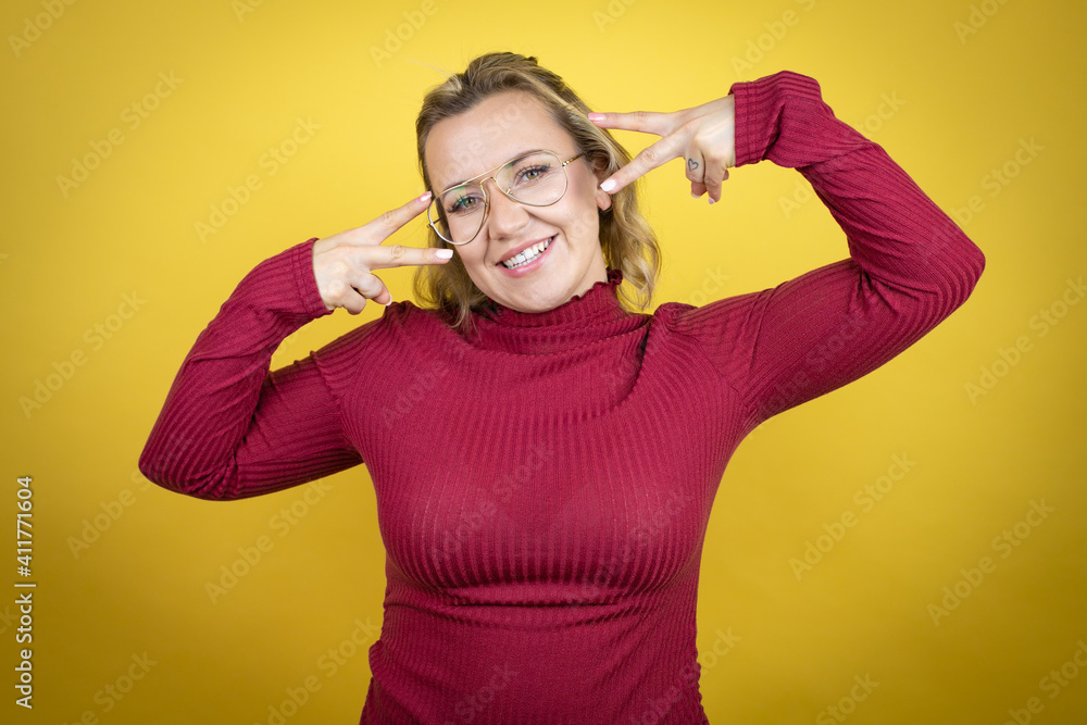 Young caucasian woman wearing casual red t-shirt over yellow background Doing peace symbol with fingers over face, smiling cheerful showing victory Young caucasian woman wearing casual red t-shirt over yellow background Doing peace symbol with fingers over face, smiling cheerful showing victory