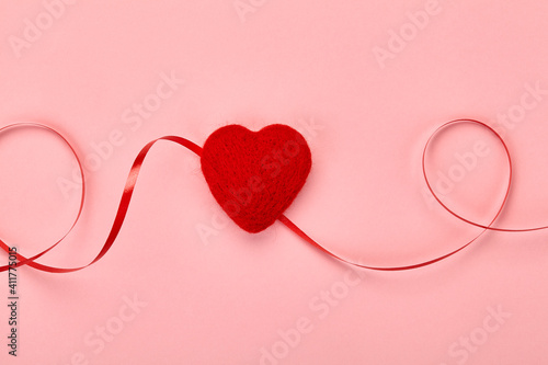 A red hand-made heart on a pink background satin ribbon view from above