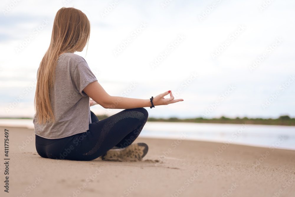 young woman practices yoga sitting on the beach in lotus position and hands folded in jnana mudra. copy space