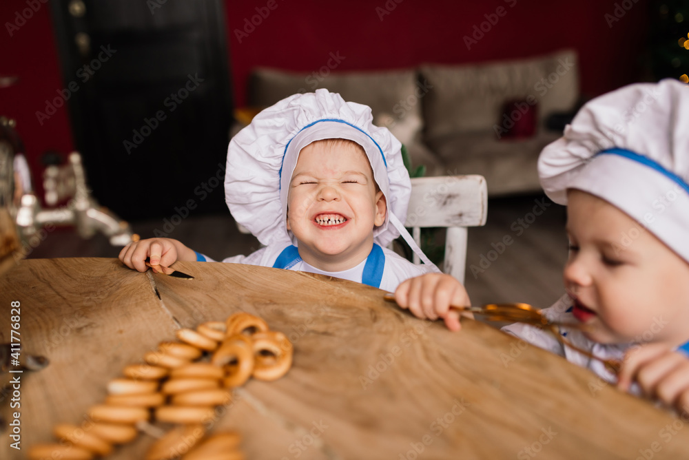 Little cute cook with cutlery sitting on a kitchen, twin brothers, tangerine, bagels Little cute cook with cutlery sitting on a kitchen, twin brothers, tangerine, bagels