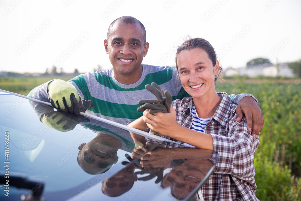 Smiling woman and man farm workers posing together standing near car outdoors