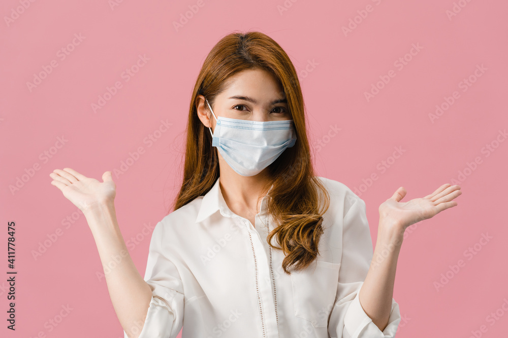 Young Asia girl wearing medical face mask showing peace sign, encourage with dressed in casual cloth and looking at camera isolated on pink background. Social distancing, quarantine for corona virus.