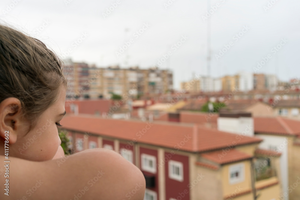 Girl leaning on the terrace ledge observes the street through the confinement of covid-19. Concept of social distancing.