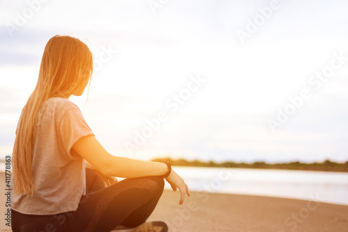Fotografija young woman practices yoga sitting on the beach in lotus position and hands folded in jnana mudra