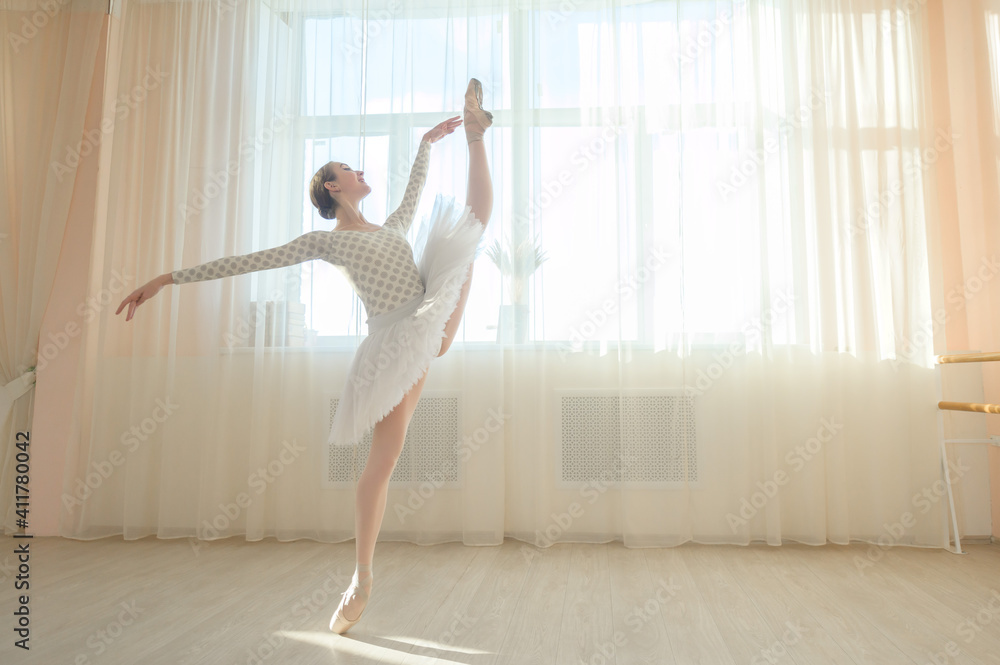 Beautiful ballerina in body and white tutu is training in a dance class. Young flexible dancer posing in pointe shoes. Beautiful ballerina in body and white tutu is training in a dance class. Young flexible dancer posing in pointe shoes.