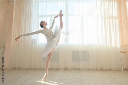 Beautiful ballerina in body and white tutu is training in a dance class. Young flexible dancer posing in pointe shoes.