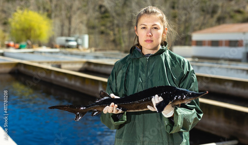 Photography Woman in working clothes standing near fish pools and holding sturgeon