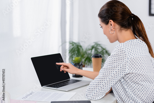 businesswoman pointing with finger at laptop with blank screen in office
