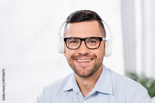 happy businessman in glasses and wireless headphones smiling while looking at camera